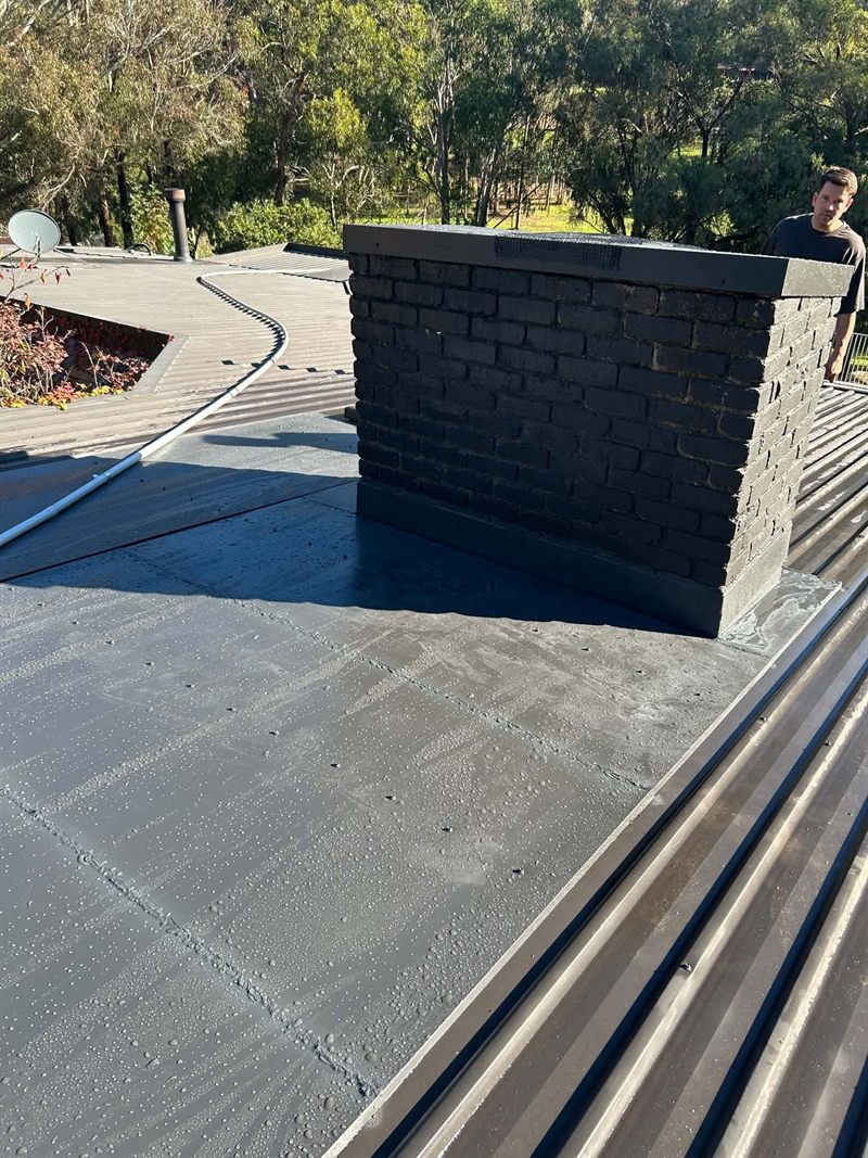 Sealed roof membrane and box gutter run around a brick chimney on a metal roof