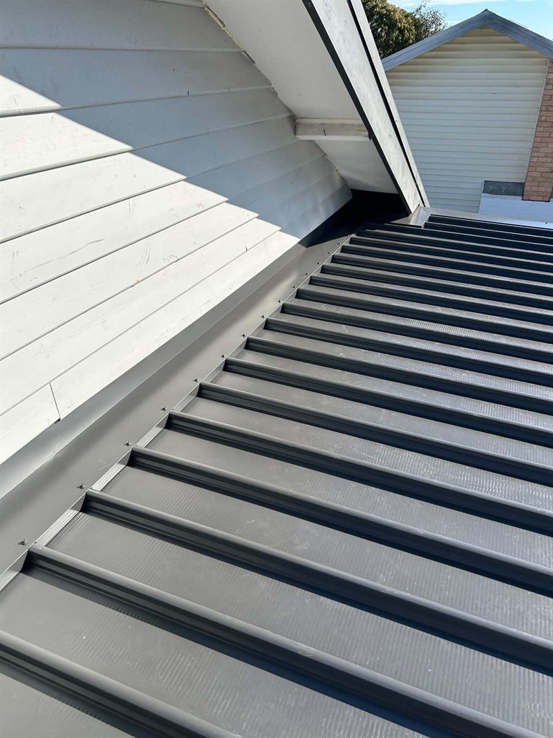 New metal roof sheeting running up to a wall with apron flashing fixed along the join