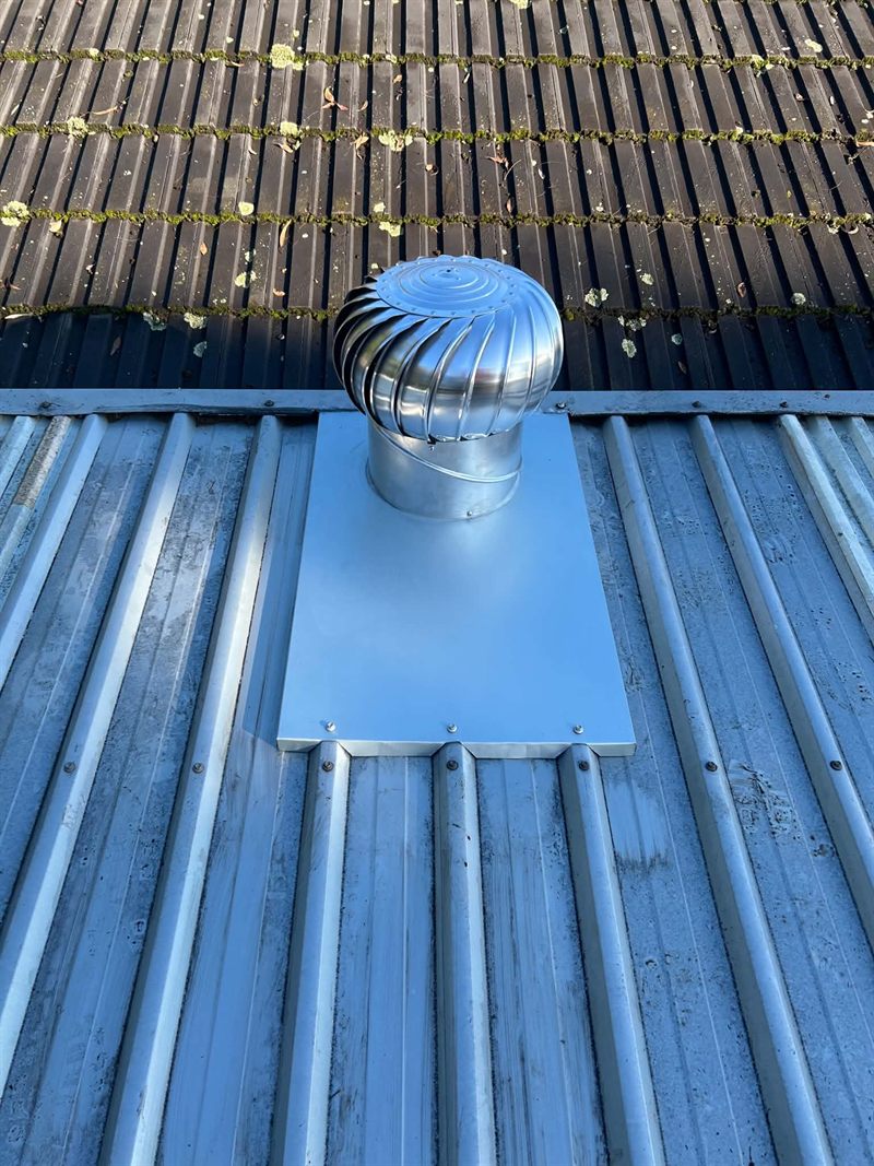New whirlybird roof vent installed on a fresh flashing tray, the older mossy roof section visible above it